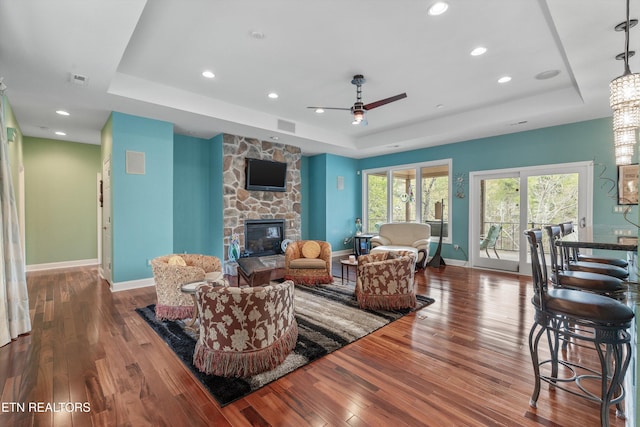 living area with hardwood / wood-style flooring, a ceiling fan, a stone fireplace, and a raised ceiling