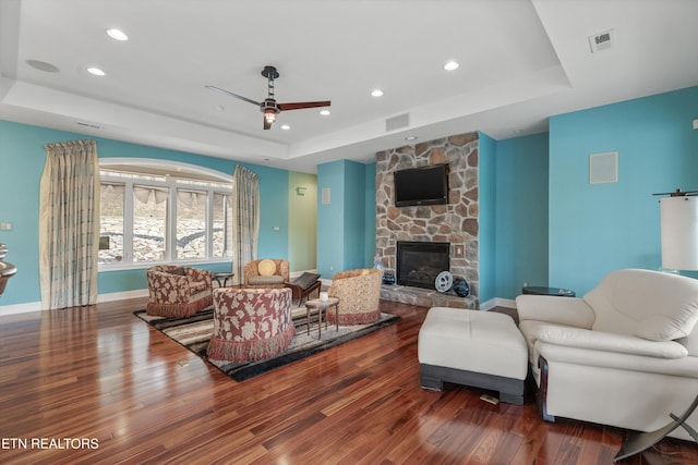 living area featuring a tray ceiling, wood finished floors, visible vents, and ceiling fan