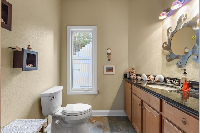 bathroom with stone tile floors, toilet, baseboards, and vanity
