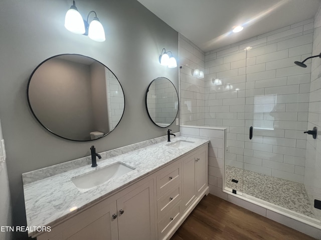 full bath with wood finished floors, a sink, double vanity, and a stall shower