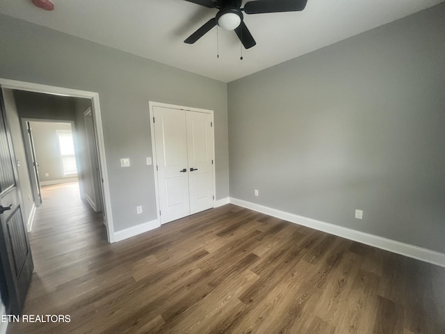unfurnished bedroom featuring dark wood-type flooring, a closet, a ceiling fan, and baseboards