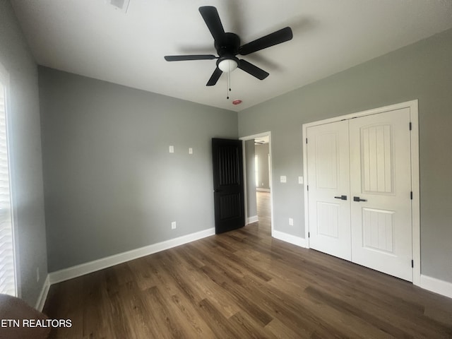 unfurnished bedroom with dark wood finished floors, a closet, baseboards, and ceiling fan