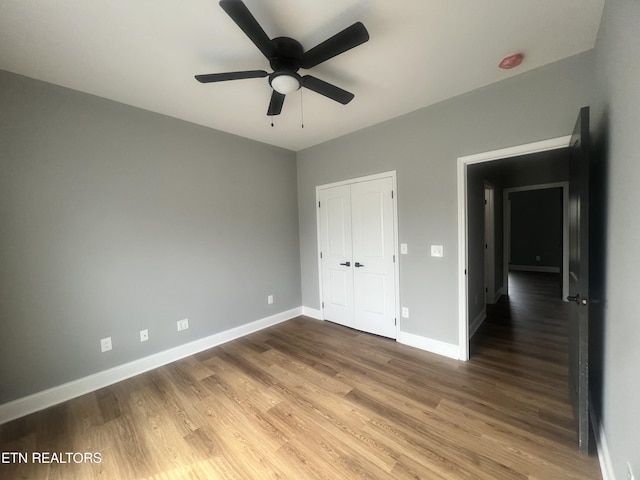 unfurnished bedroom with ceiling fan, baseboards, wood finished floors, and a closet