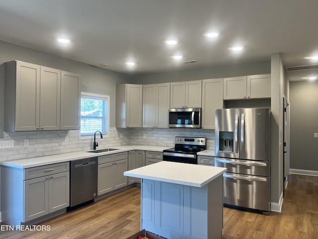 kitchen with light countertops, a sink, decorative backsplash, gray cabinetry, and appliances with stainless steel finishes