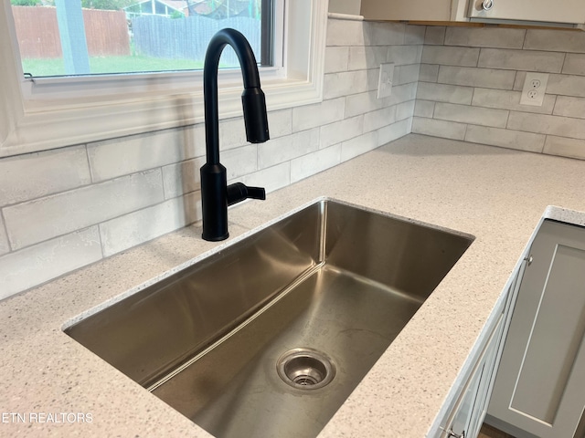 room details featuring light stone countertops, decorative backsplash, a sink, and gray cabinets