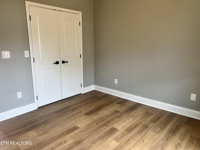unfurnished bedroom with a closet, baseboards, and dark wood-style floors