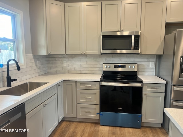kitchen featuring a sink, light wood-style floors, backsplash, appliances with stainless steel finishes, and gray cabinetry