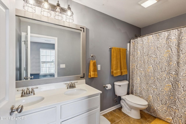 bathroom with baseboards, toilet, double vanity, and a sink
