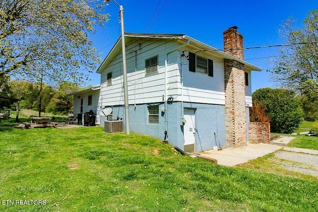 back of house featuring central air condition unit, a lawn, and a chimney