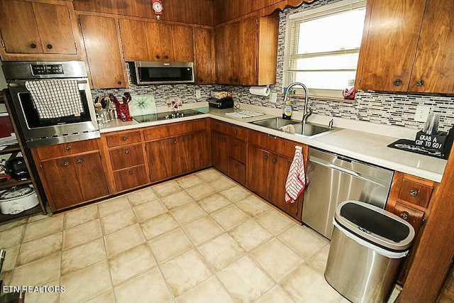 kitchen with appliances with stainless steel finishes, tasteful backsplash, a sink, and light countertops