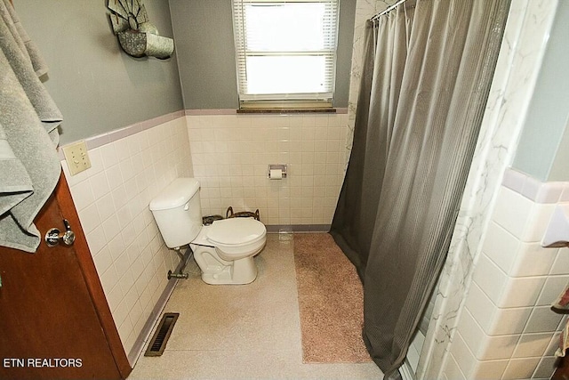 full bathroom featuring a wainscoted wall, toilet, tile walls, visible vents, and curtained shower