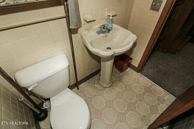 half bath featuring toilet, tile patterned floors, and tile walls