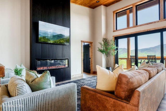 interior space with a towering ceiling, wood ceiling, a glass covered fireplace, and wood finished floors