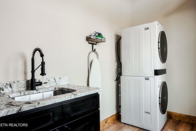 laundry area featuring stacked washer and clothes dryer, baseboards, light wood-style flooring, and a sink