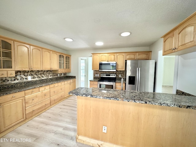 11709 Black Powder Dr, Knoxville, TN 37934 - kitchen with light wood-style flooring, tasteful backsplash, glass insert cabinets, light brown cabinets, and appliances with stainless steel finishes