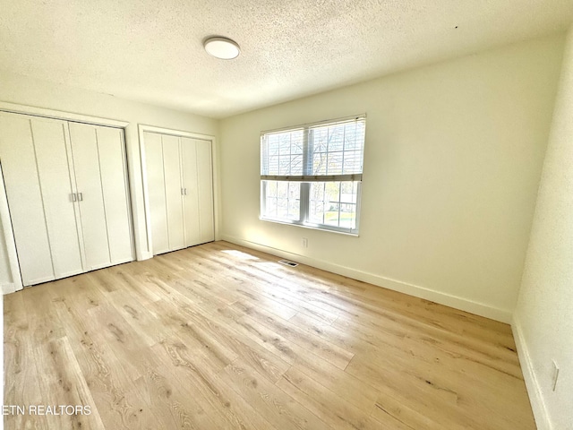 11709 Black Powder Dr, Knoxville, TN 37934 - unfurnished bedroom featuring light wood-type flooring, baseboards, a textured ceiling, and two closets