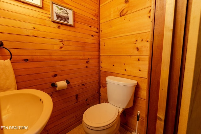 half bathroom featuring a sink, wood walls, and toilet