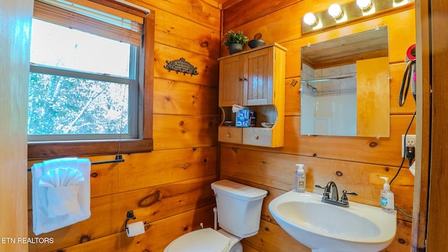 bathroom featuring toilet, wood walls, plenty of natural light, and a sink