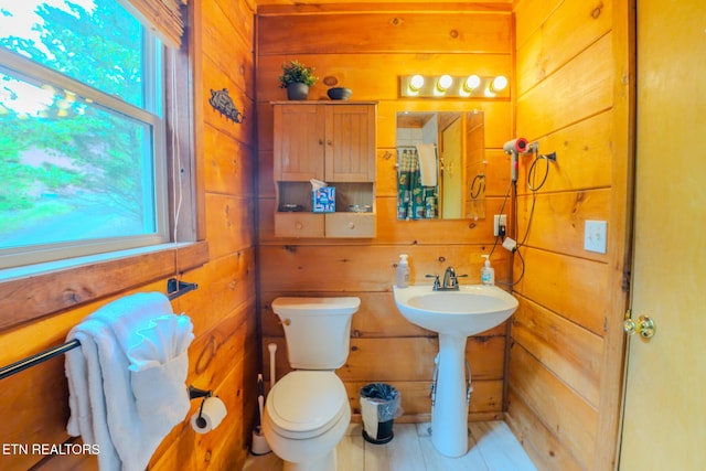 half bathroom featuring a sink, tile patterned floors, wooden walls, and toilet