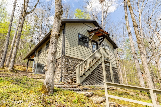 exterior space with central air condition unit, stairway, and stone siding