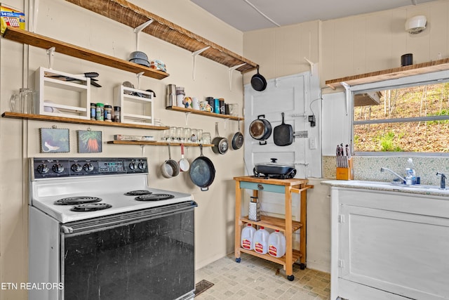 kitchen featuring electric range, baseboards, light countertops, white cabinets, and a sink
