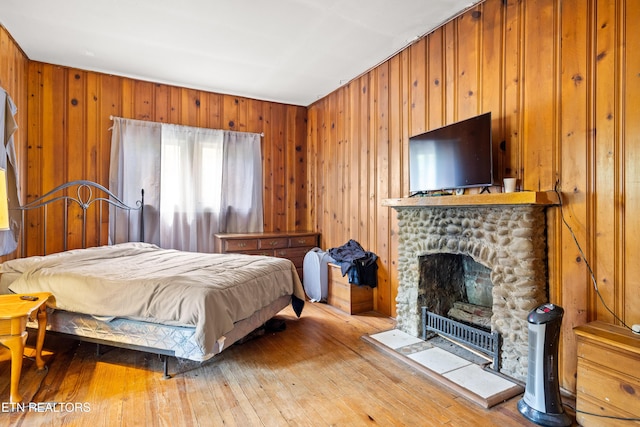 bedroom with wooden walls, wood-type flooring, and a stone fireplace