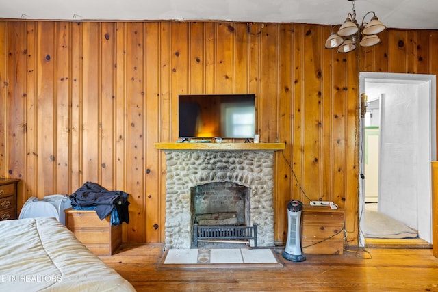 living area with an inviting chandelier, wood-type flooring, wooden walls, and a stone fireplace