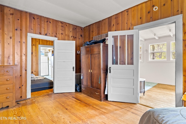 bedroom featuring freestanding refrigerator, wood walls, and light wood finished floors