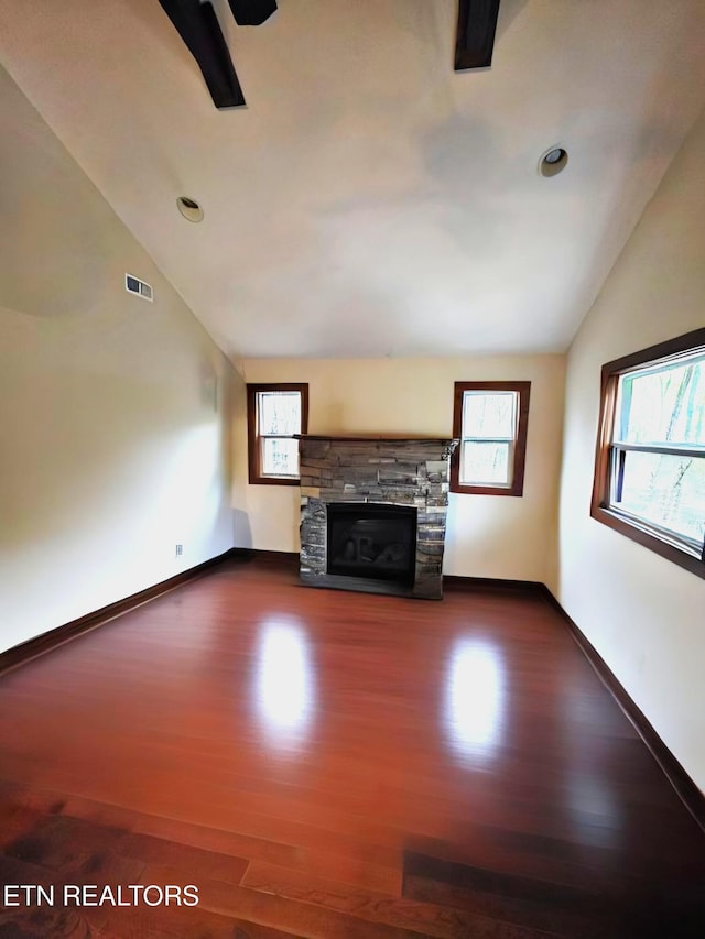 unfurnished living room featuring visible vents, lofted ceiling, baseboards, a stone fireplace, and dark wood-style floors