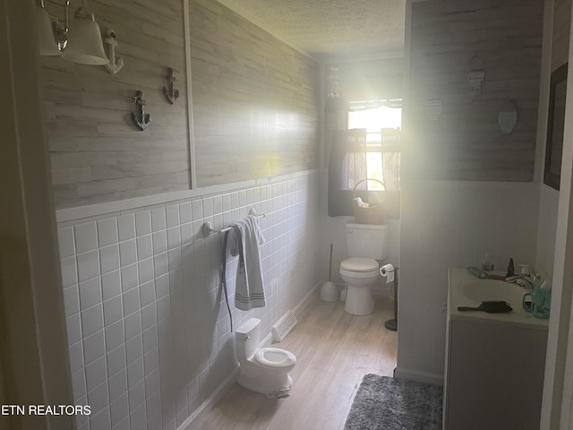 bathroom with a tile shower, a wainscoted wall, wood finished floors, toilet, and a textured ceiling