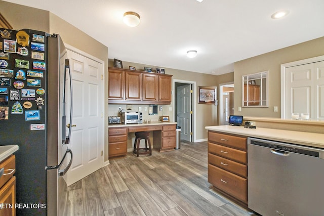 kitchen with brown cabinetry, stainless steel appliances, a toaster, light countertops, and light wood finished floors
