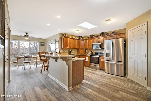 kitchen featuring brown cabinetry, stainless steel appliances, light countertops, light wood finished floors, and a peninsula