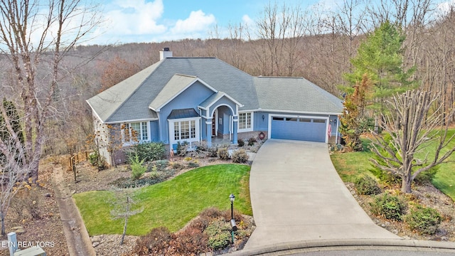 ranch-style home featuring a chimney, a garage, driveway, roof with shingles, and a front lawn