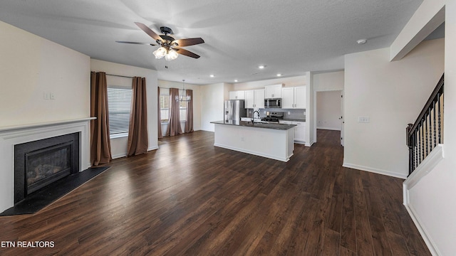 kitchen with ceiling fan, dark countertops, appliances with stainless steel finishes, a sink, and an island with sink