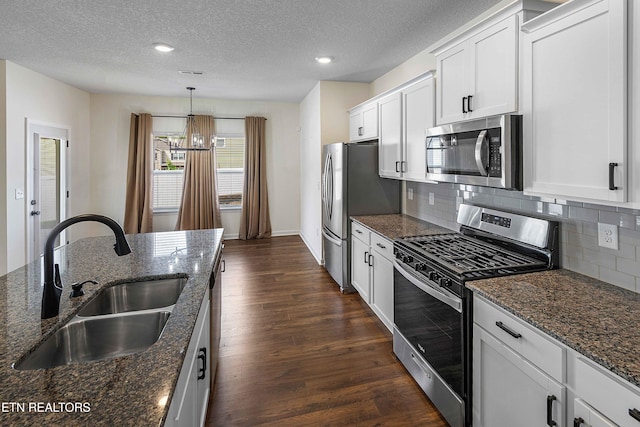 kitchen featuring backsplash, a textured ceiling, appliances with stainless steel finishes, a sink, and a notable chandelier