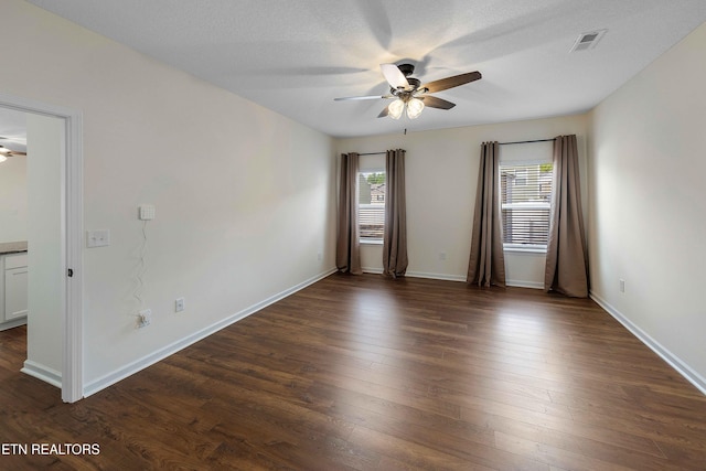 spare room with baseboards, a ceiling fan, dark wood-style flooring, and visible vents