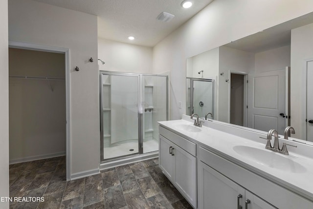 full bathroom with double vanity, a sink, a spacious closet, and a shower stall