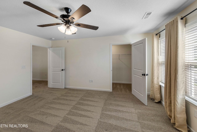 unfurnished bedroom with a walk in closet, a textured ceiling, visible vents, baseboards, and carpet