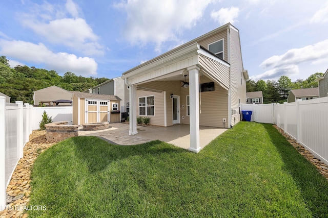 back of property with a storage unit, a fenced backyard, a ceiling fan, and an outbuilding