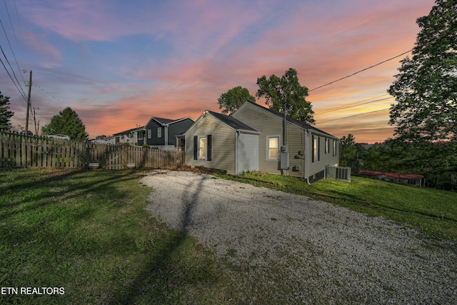 property exterior at dusk with fence, a yard, and central AC unit