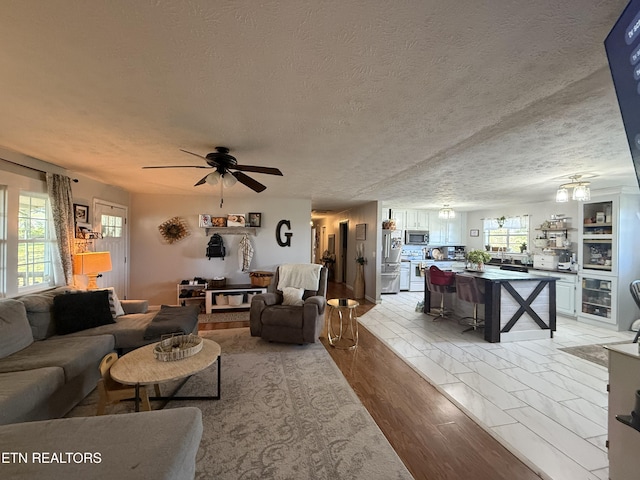 living area featuring light wood finished floors, a textured ceiling, a ceiling fan, and wine cooler