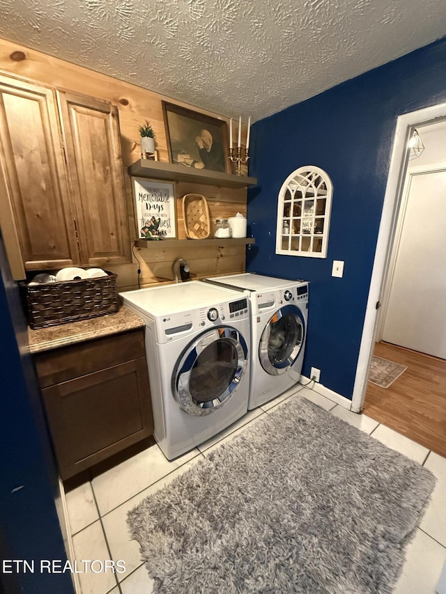 laundry room with cabinet space, light tile patterned floors, washer and clothes dryer, and a textured ceiling