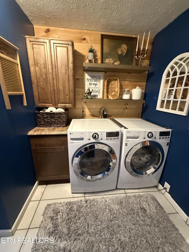 clothes washing area with light tile patterned floors, independent washer and dryer, a textured ceiling, baseboards, and cabinet space