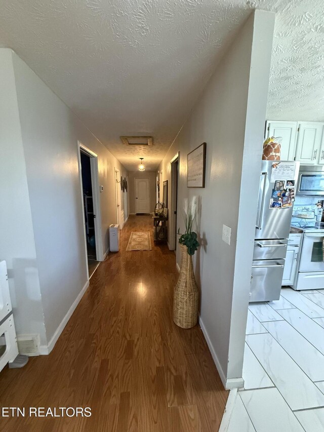 hall featuring light wood-type flooring, baseboards, and a textured ceiling