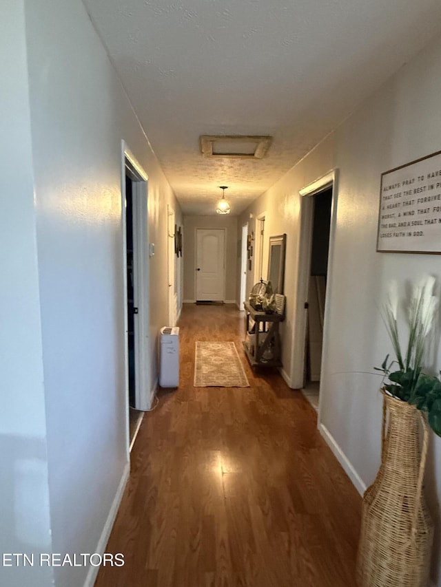 corridor with baseboards, attic access, and wood finished floors