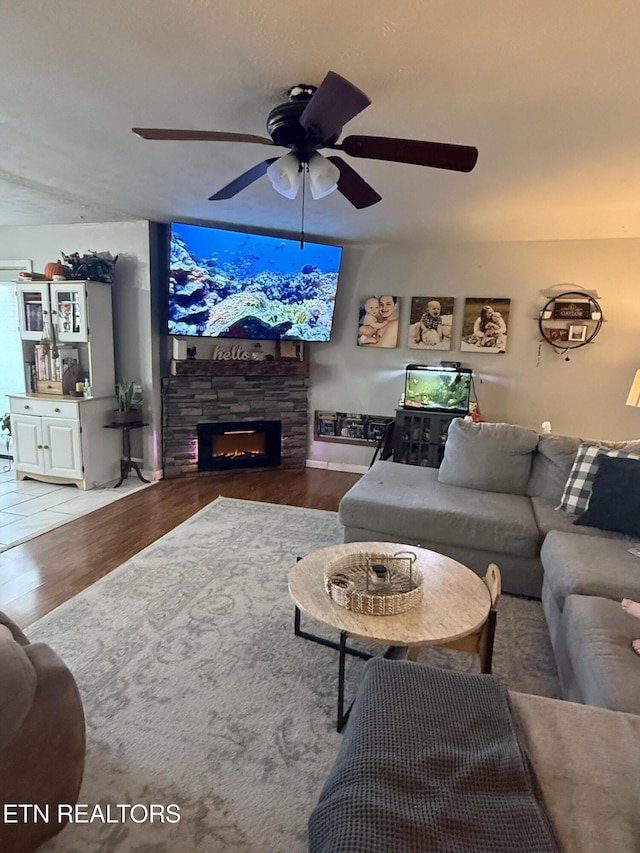 living room featuring ceiling fan, a stone fireplace, and wood finished floors