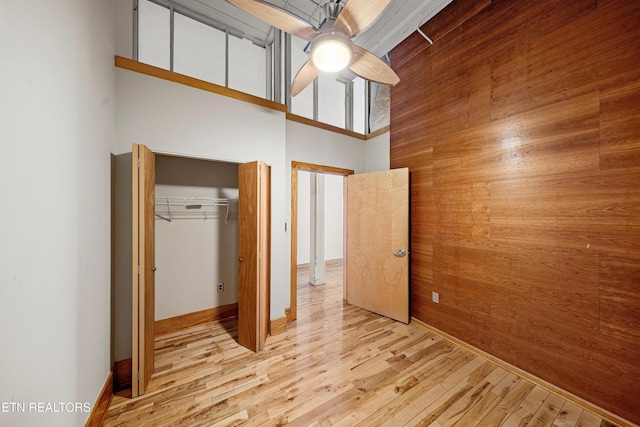 unfurnished bedroom featuring a ceiling fan, wood walls, wood finished floors, a high ceiling, and a closet