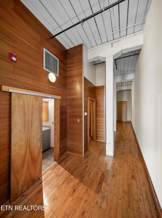 corridor featuring visible vents, a towering ceiling, wooden walls, and light wood-style flooring