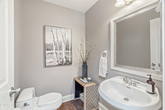 half bathroom with wood finished floors, toilet, baseboards, and a sink
