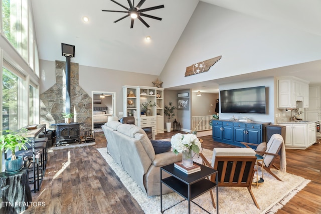 living room with dark wood-type flooring, a wood stove, a ceiling fan, and high vaulted ceiling